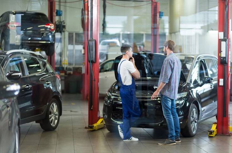 Two men in a garage with cars on the floor.